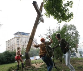 FEMEN protester hacking off a cross in a park.